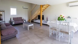 A modern living room with a staircase, a sofa, a coffee table, and a dining area with a white table and chairs.