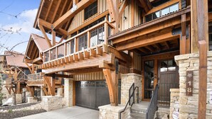 A multi-story wooden house with a stone foundation, a garage, and a staircase leading to the entrance.