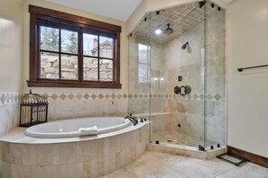 A bathroom with a freestanding bathtub, a glass-enclosed shower, and a window with a stone wall view.