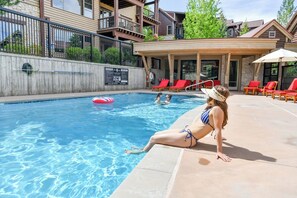 A swimming pool with a lounge area, red chairs, and a covered seating area.