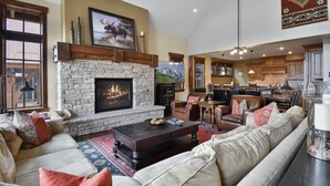 A spacious living room with a stone fireplace, leather sofas, and a large television.