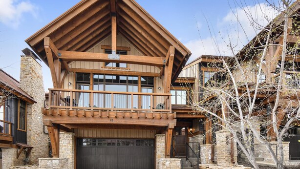 A multi-story log cabin with a stone foundation, a large garage door, and a balcony.