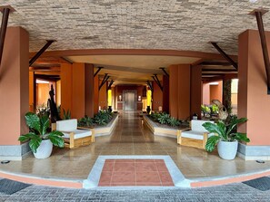 A hotel lobby with a central corridor, seating areas, and potted plants.