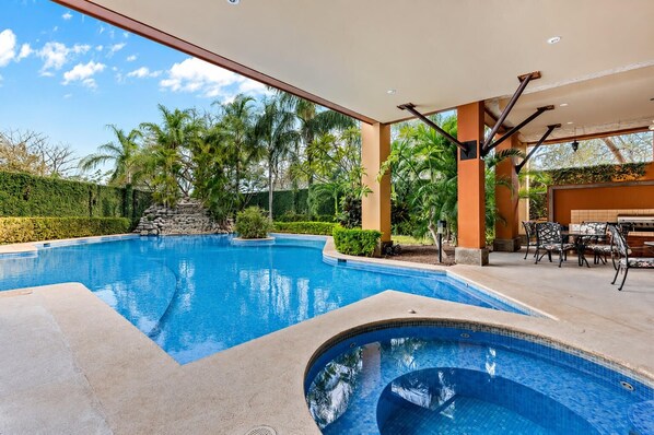 A swimming pool with a patio area, outdoor seating, and a view of the surrounding greenery.