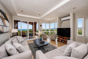 Un salón amplio con un televisor grande, asientos cómodos, una mesa de centro y vistas al océano.