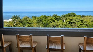 Een balkon met drie houten stoelen en uitzicht op zee en tropische begroeiing.