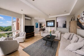 A spacious living room with a large TV, comfortable seating, and a view of greenery outside. - Amazing Ocean View Condo Close to the Beach w/Free Pickleball <br><br>Exclusive Pickleball Benefit:<br><br>As our guest, you'll receive complimentary pickleball access at 15 Love in Tamarindo. (Up to<br>two hours per day.) (Playa Langosta)