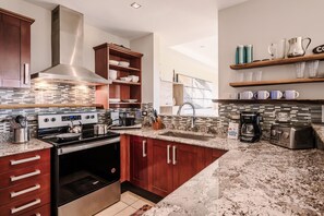 Una cocina moderna con encimeras de granito, electrodomésticos de acero inoxidable, armarios de madera y un salpicadero con diseño de mosaico.