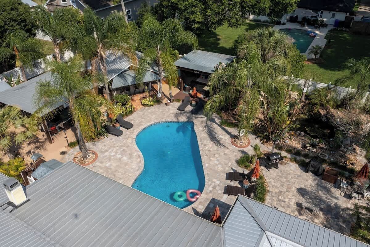 Ett flygbildsbild av ett bostadsområde med en swimmingpool, utemöbler och omgivande grönska.