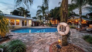 A pool area with a lifebuoy, palm trees, and a building with lights.