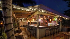 An outdoor bar area with a counter, bar stools, string lights, and a covered seating area.
