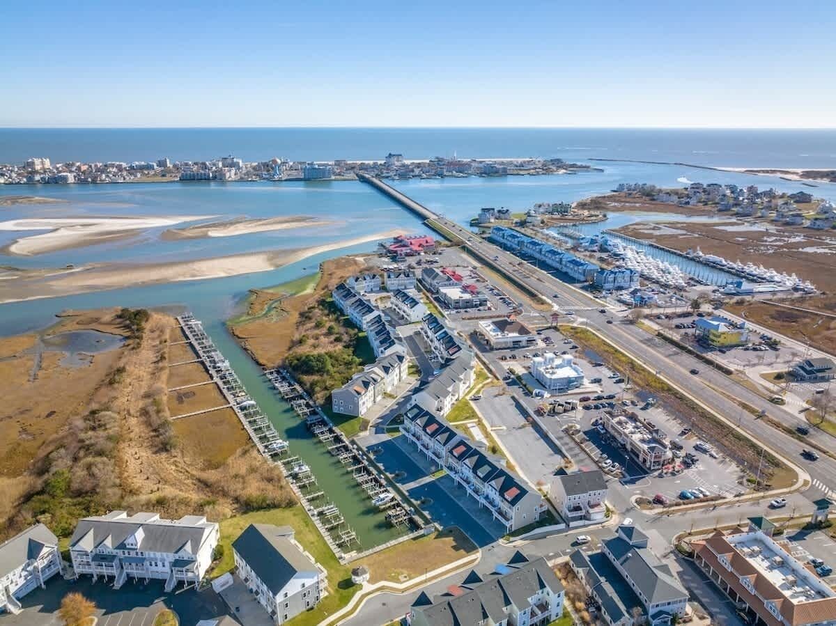 An aerial view of a coastal area with a marina, residential buildings, and a long pier extending into the water.