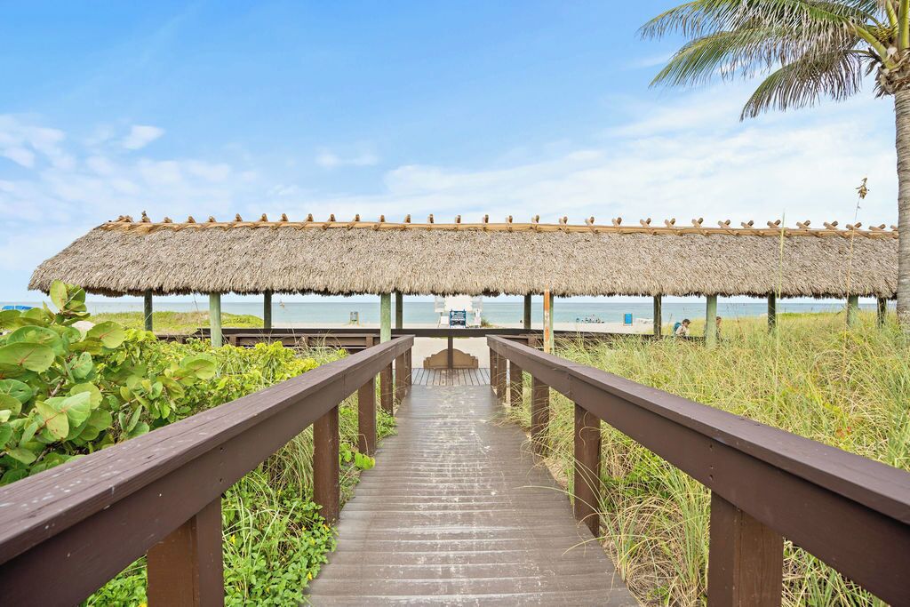 A wooden pathway leading to a thatched-roof structure by the water.
