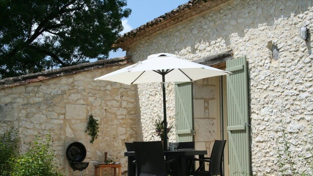 Eine Terrasse im Freien mit Tisch, Stühlen, einem Grill und einer Steinmauer.
