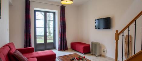 A living room with a red sofa, a wooden coffee table, a TV mounted on the wall, and a staircase.
