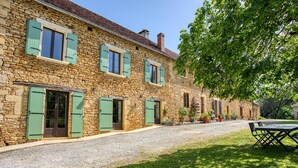 A stone building with green shutters, a gravel driveway, and outdoor seating.