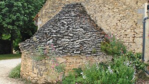 A stone building with a sloped roof, surrounded by greenery and a gravel path.