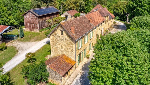A stone building with a sloped roof, surrounded by lush greenery and a dirt path.