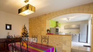 A dining area with a table set for four, a Christmas tree, and a kitchen visible through an archway.