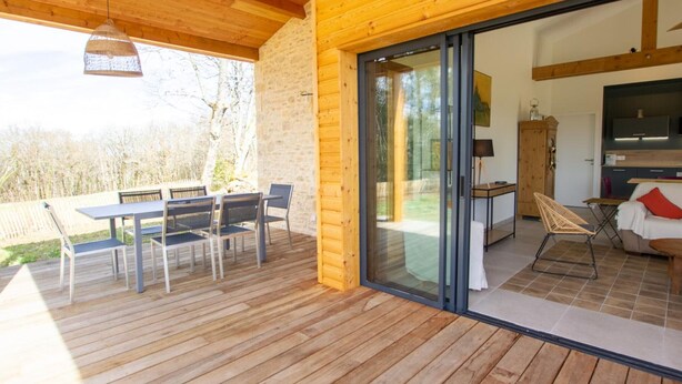 A wooden deck with a table and chairs, a sliding glass door leading to a living area with a sofa and a TV.