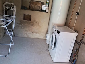 A laundry room with a washing machine, a drying rack, and a shelf with various items.