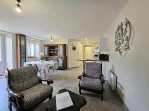 A living room with two patterned armchairs, a dining table, and a kitchen area in the background.