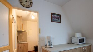Een kleine keuken met houten kastjes, een magnetron, een koffiezetapparaat en een klok aan de muur.