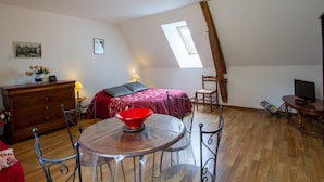 Een gezellige kamer met een bed, een houten dressoir, een eettafel met stoelen, een televisie en een dakraam.