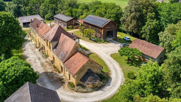 Een groot, landelijk gelegen boerderijcomplex met meerdere gebouwen, omgeven door weelderige begroeiing en een slingerende weg.