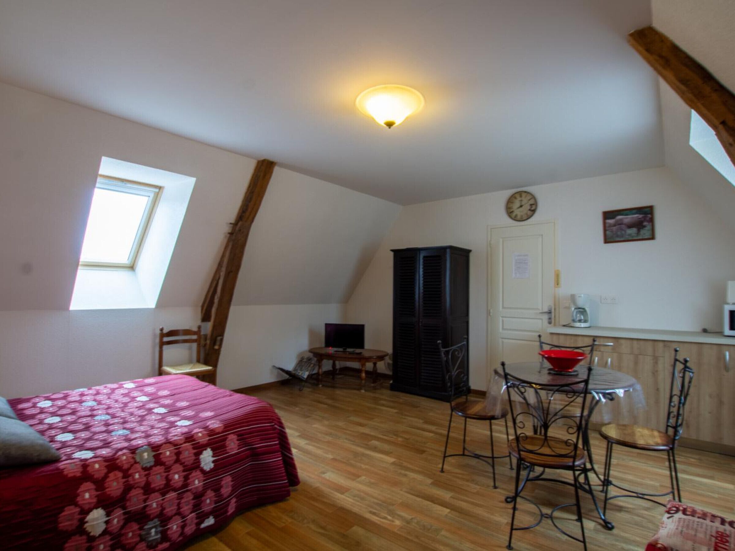 A cozy room with a bed, a small table, a chair, a clock, and a window.