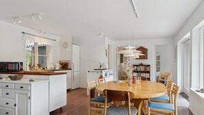 A spacious kitchen with a central island, wooden dining table with chairs, and a bookshelf in the background.