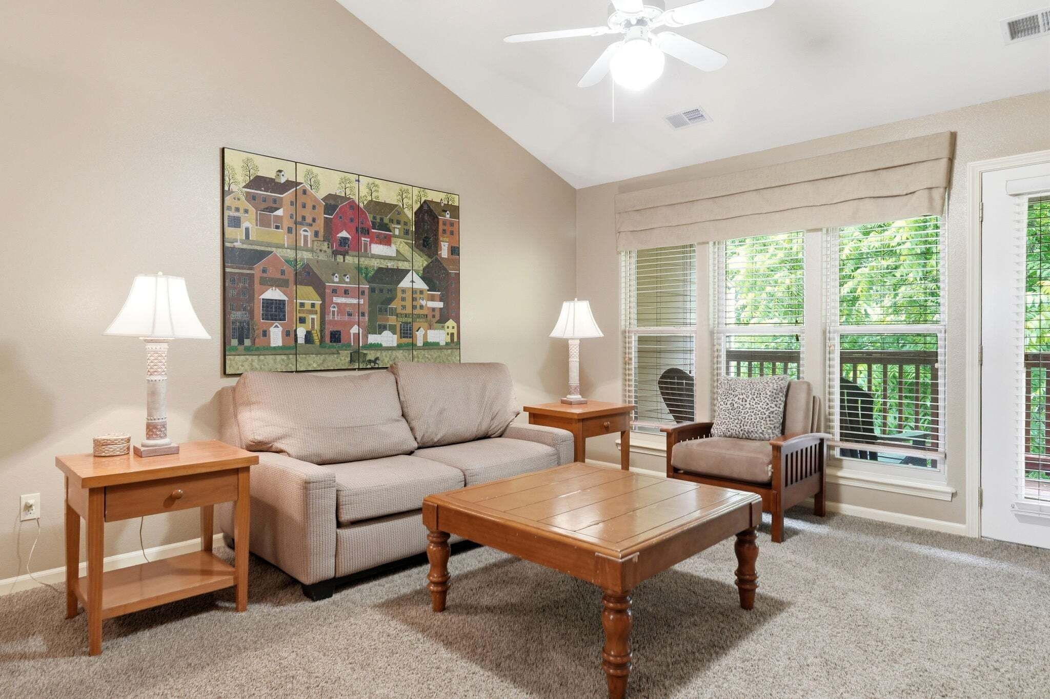A living room with a sofa, coffee table, two lamps, a painting, and a window with blinds.