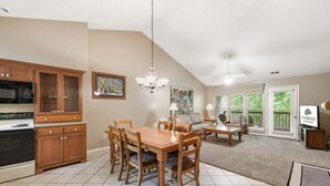 A spacious kitchen with wooden cabinets, a dining table, and chairs, a living area with a sofa and coffee table, and a view of a balcony.