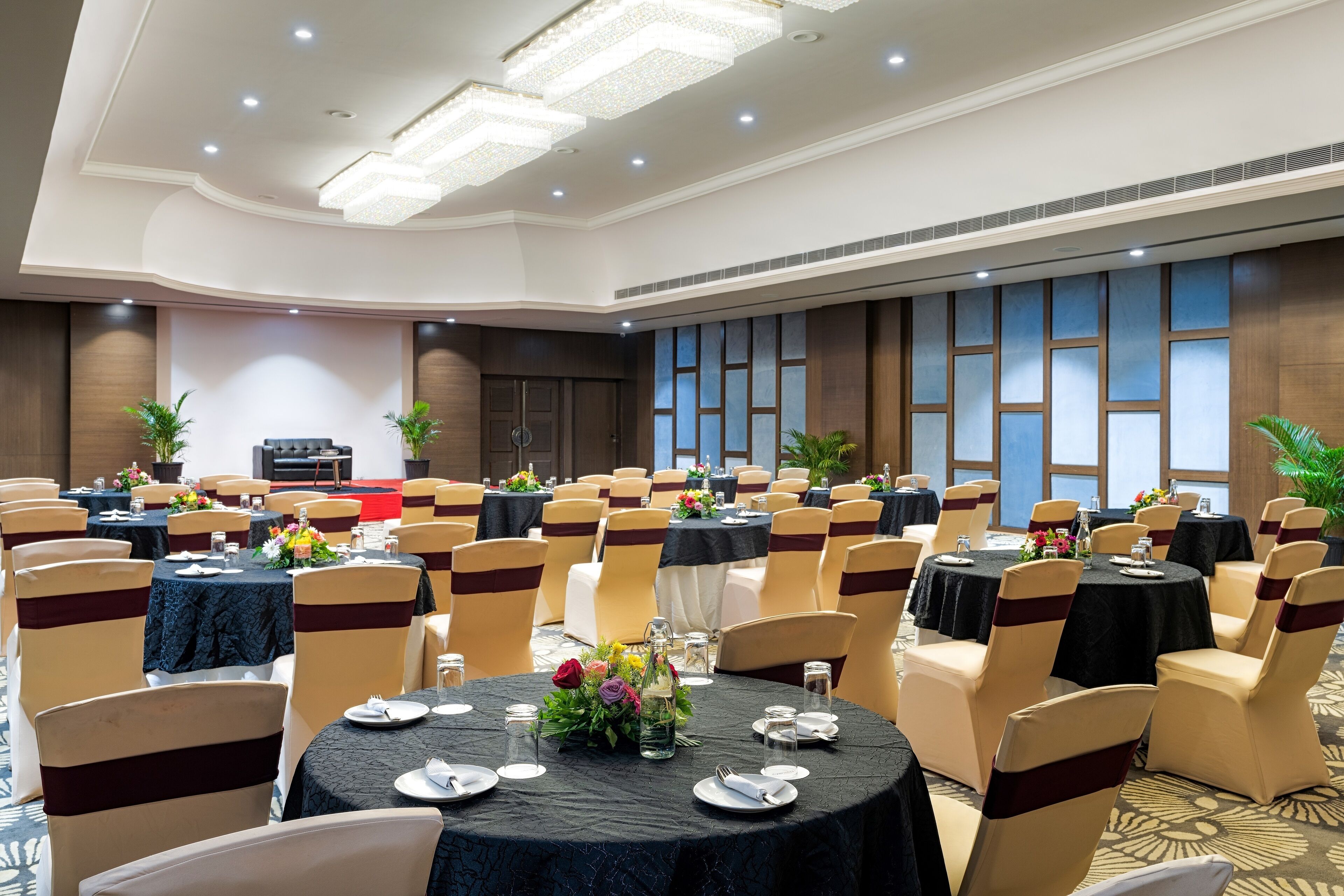A banquet hall with round tables, chairs, and floral centerpieces.