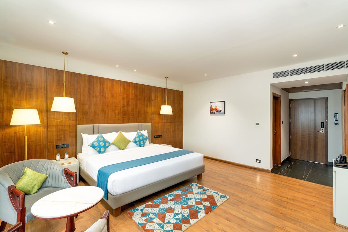 Une chambre d’hôtel avec un lit, deux lampes de chevet, un mur décoratif en bois, une petite table avec une chaise et un tapis à motifs.