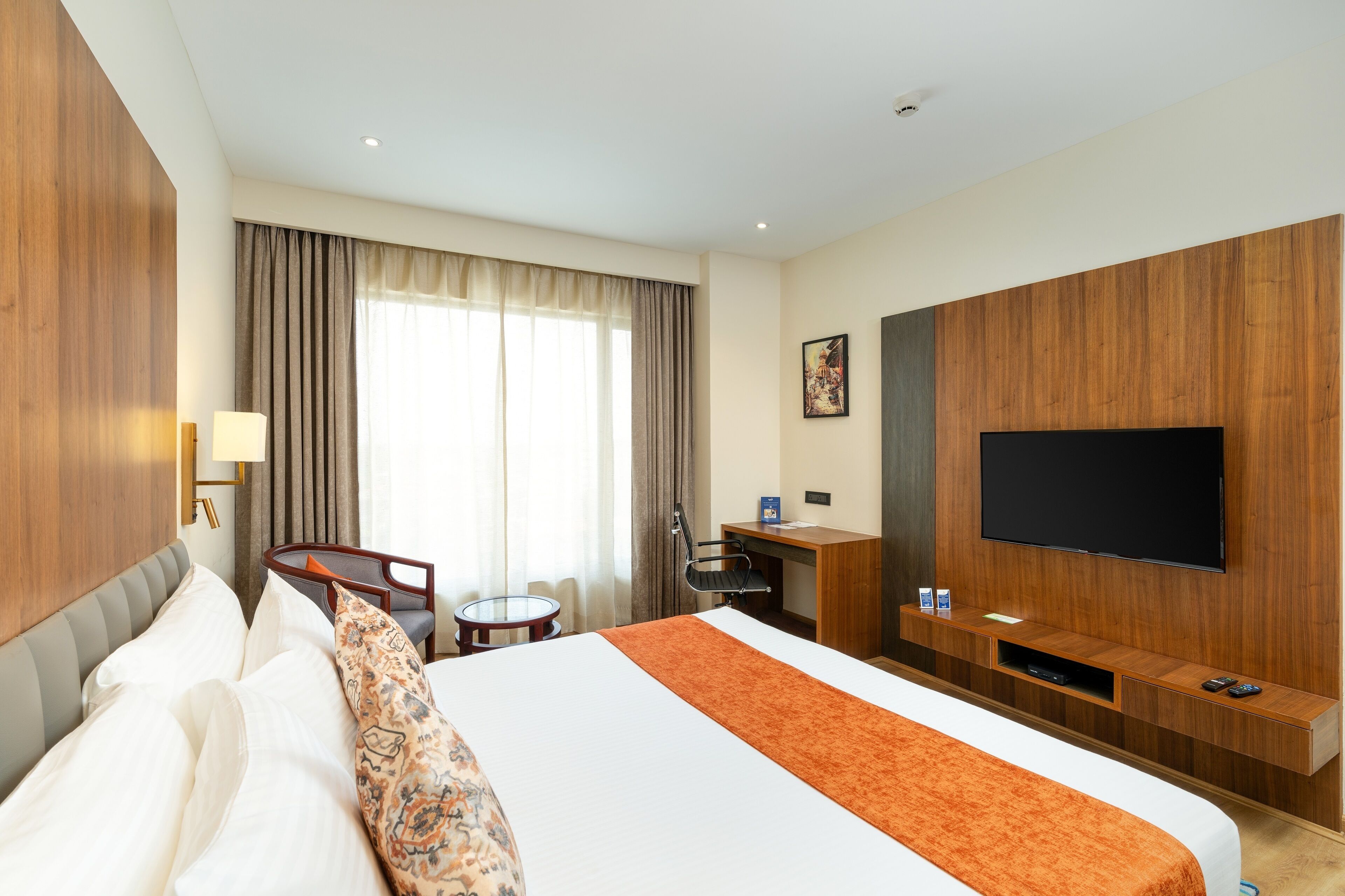 A hotel room with a large bed, a desk with a chair, a television, and a window with curtains.