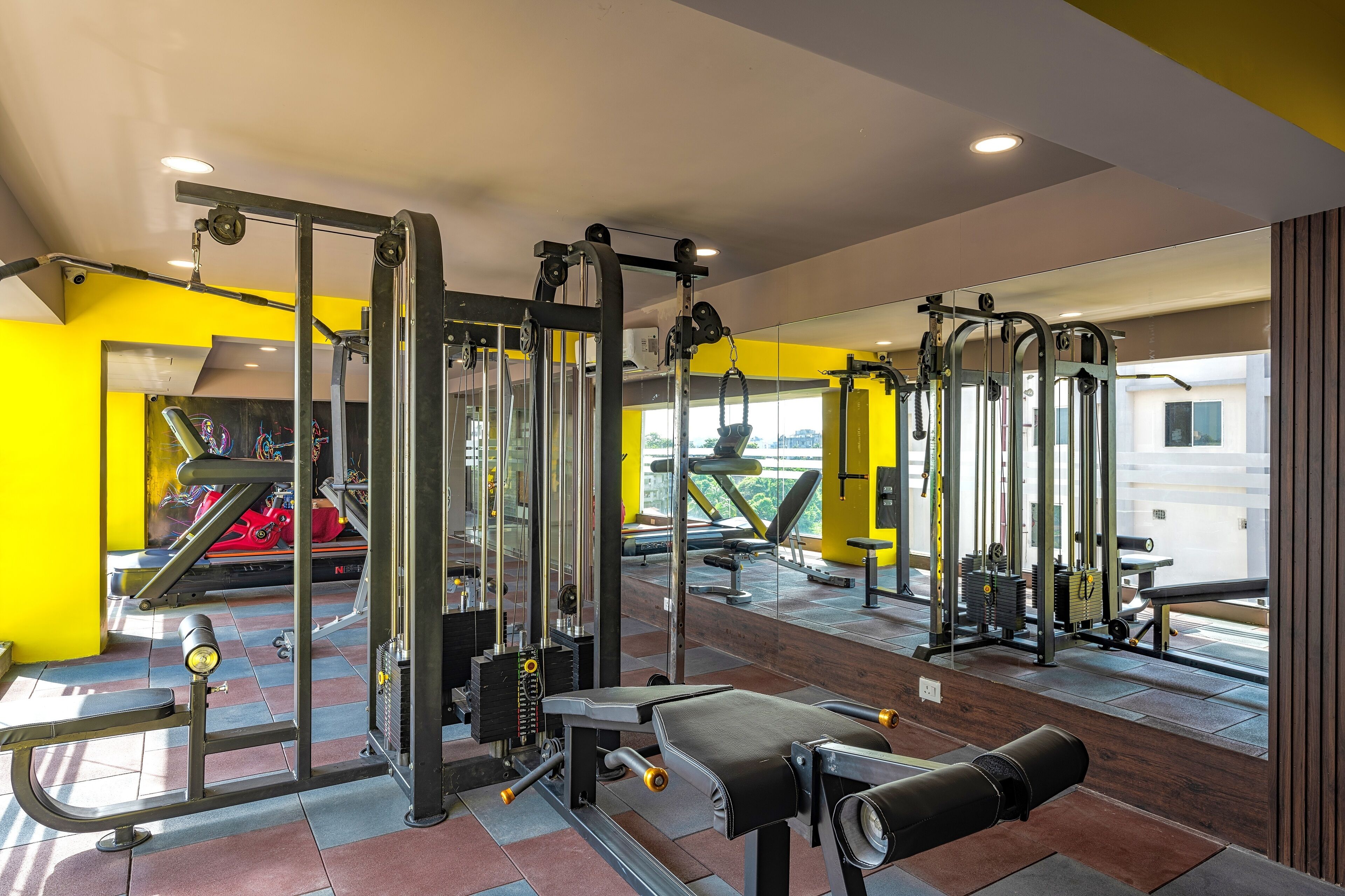 A gym with various exercise machines, a bench, and a mirror.
