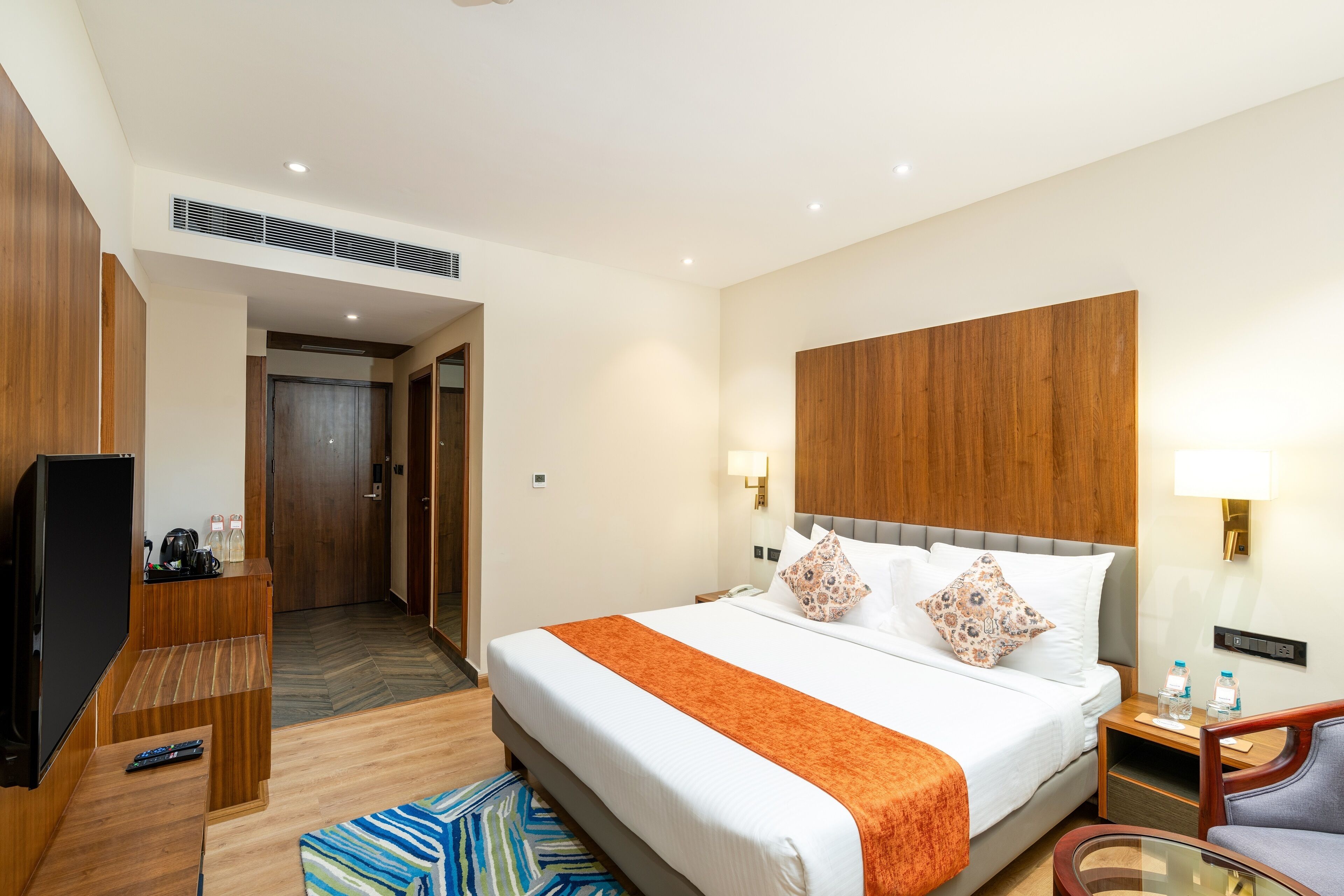 A hotel room with a large bed, wooden headboard, bedside table with lamp, and a television.