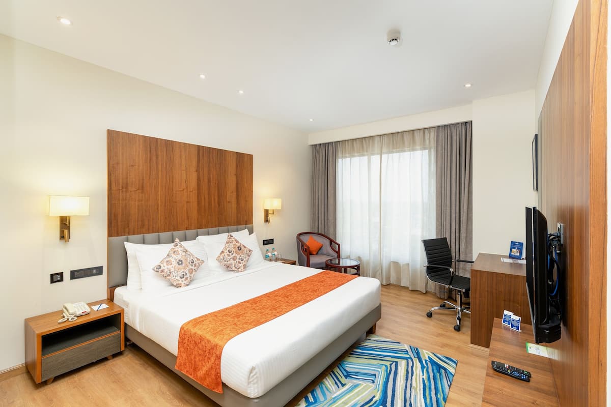 Une chambre d’hôtel avec un grand lit, des lampes de chevet, un bureau avec une télévision, une chaise et une petite table.