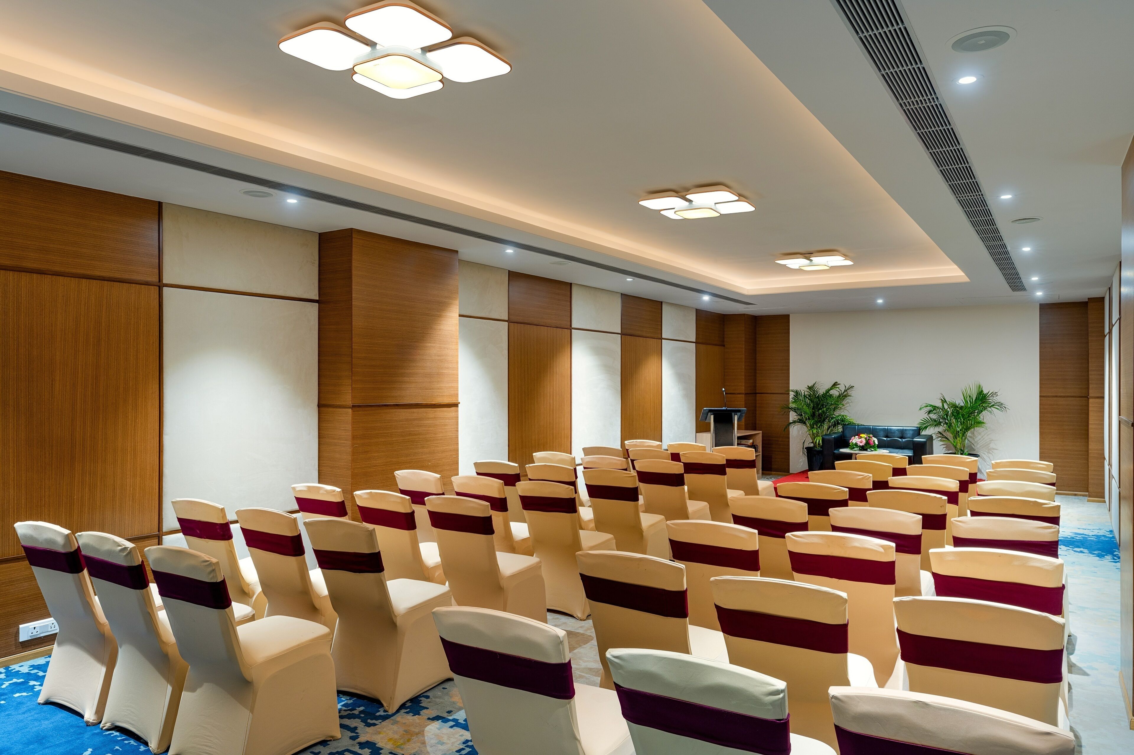 A conference room with rows of chairs, a podium, and a blue carpet.