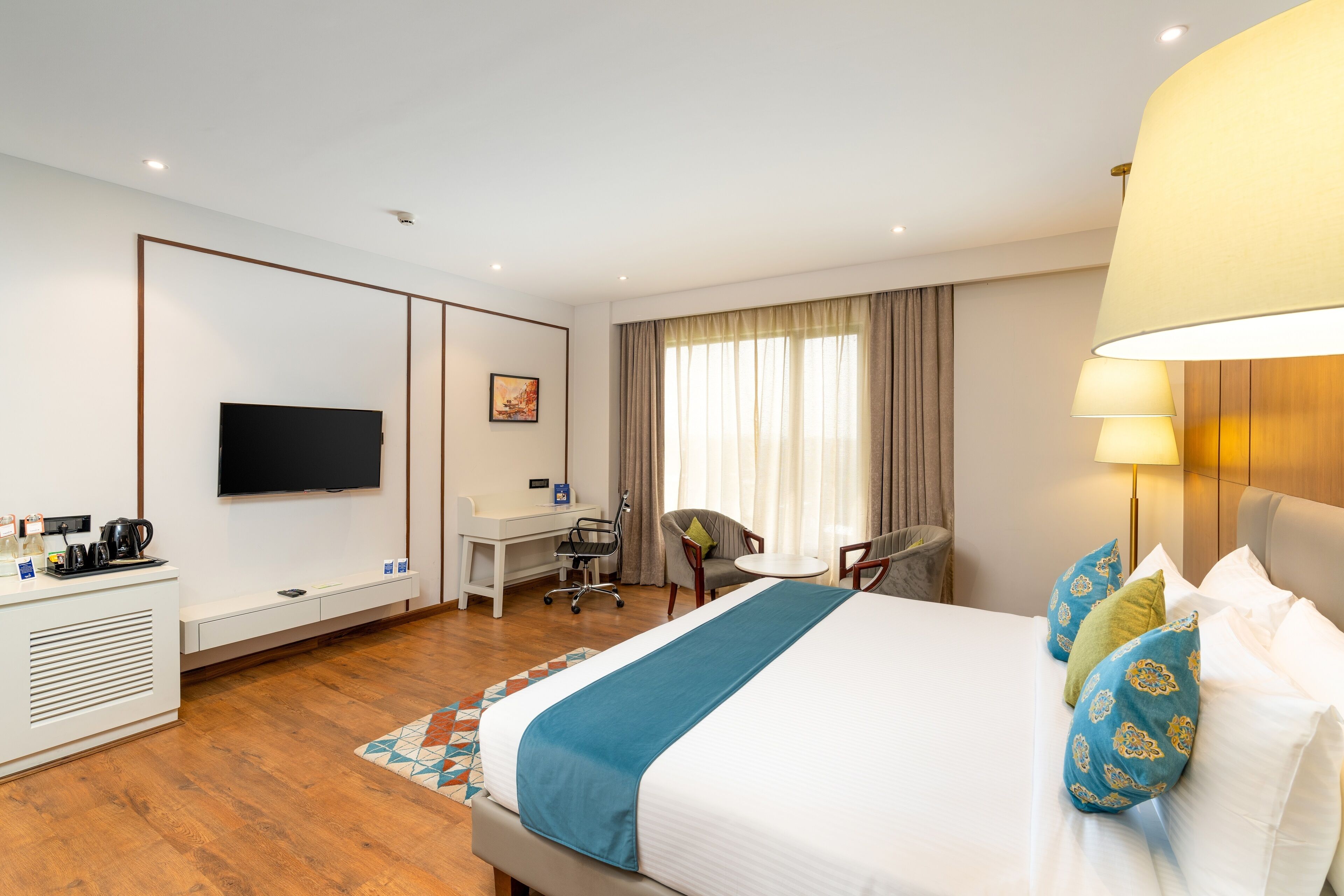 A hotel room with a large bed, a desk, a chair, a television, and a lamp.
