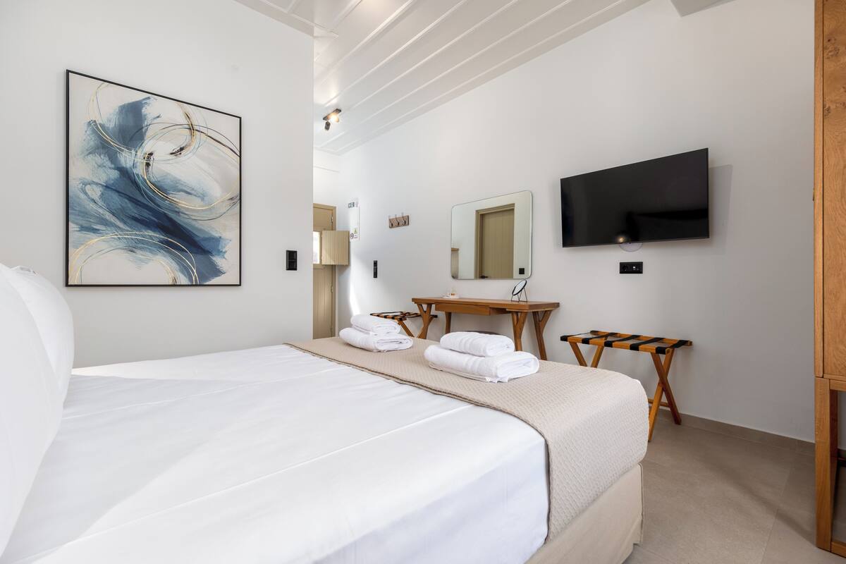 Une chambre d’hôtel avec un grand lit, un téléviseur à écran plat, un tableau, une table de chevet en bois et un miroir.
