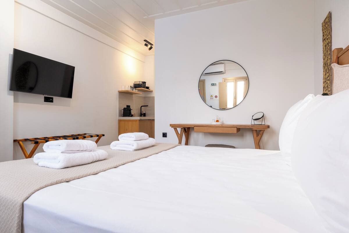 Une chambre d’hôtel équipée d’un lit, d’une télévision, d’un miroir, d’un bureau et d’une étagère avec des serviettes.