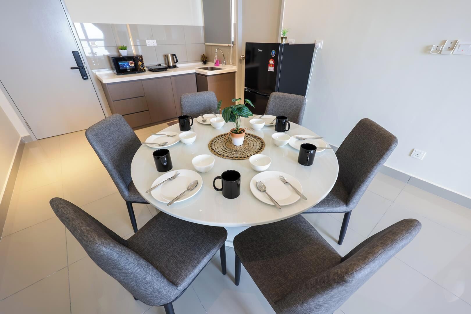A modern kitchen with a dining area, including a round table with chairs, a coffee maker, and a refrigerator.