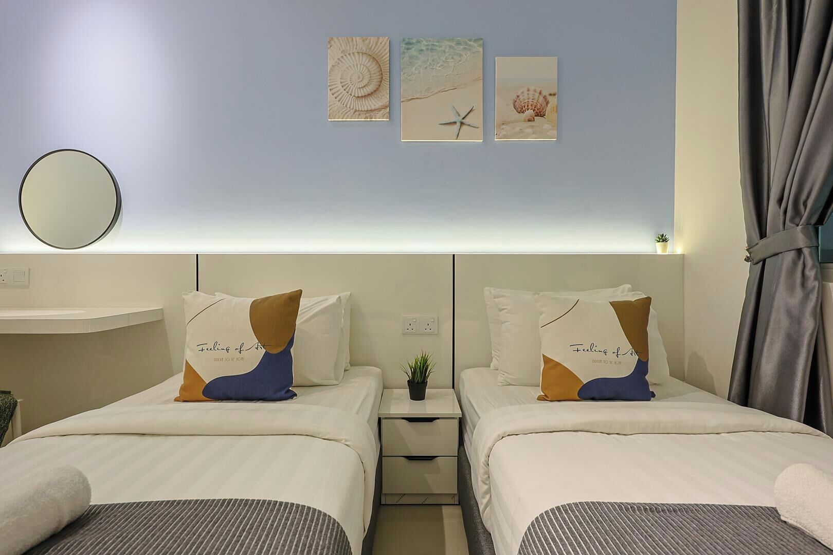 A hotel room with two beds, a bedside table with a plant, and artwork on the wall.