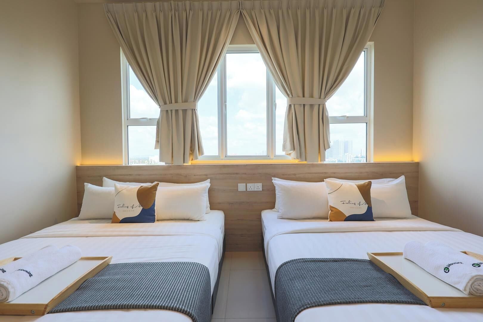A hotel room with two beds, a wooden headboard, a window with curtains, and a city view.