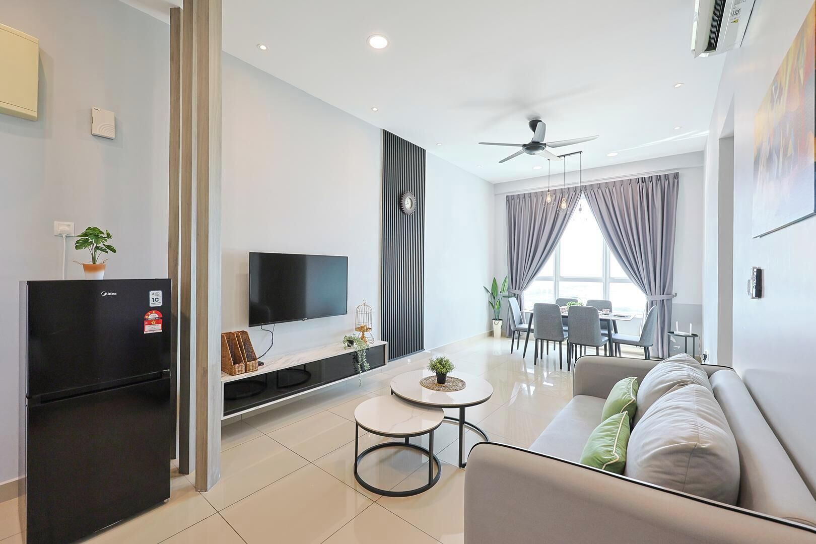 Un salon moderne doté d’un téléviseur à écran plat, d’un réfrigérateur noir, d’un canapé, d’un coin repas avec une table et des chaises, et d’un ventilateur de plafond.