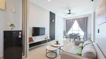 Un salon moderne doté d’un téléviseur à écran plat, d’un réfrigérateur noir, d’un canapé, d’un coin repas avec une table et des chaises, et d’un ventilateur de plafond.
