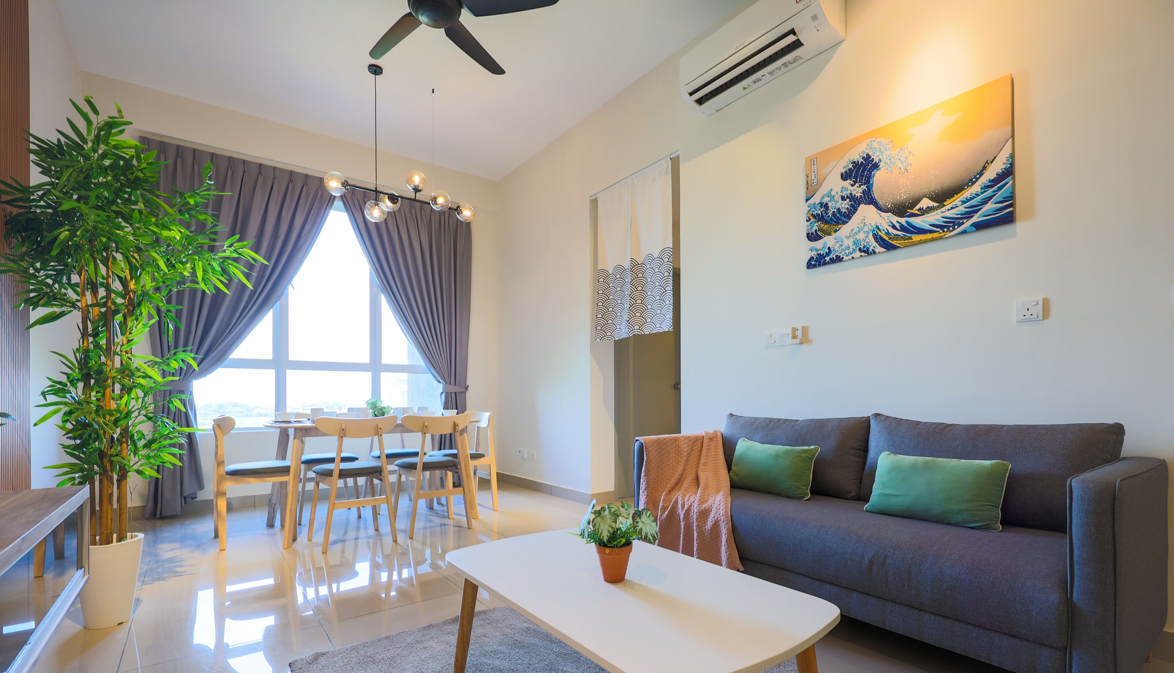 A modern living room with a sofa, a coffee table, a dining area with chairs, a large window with curtains, a ceiling fan, and a wall-mounted air conditioner.