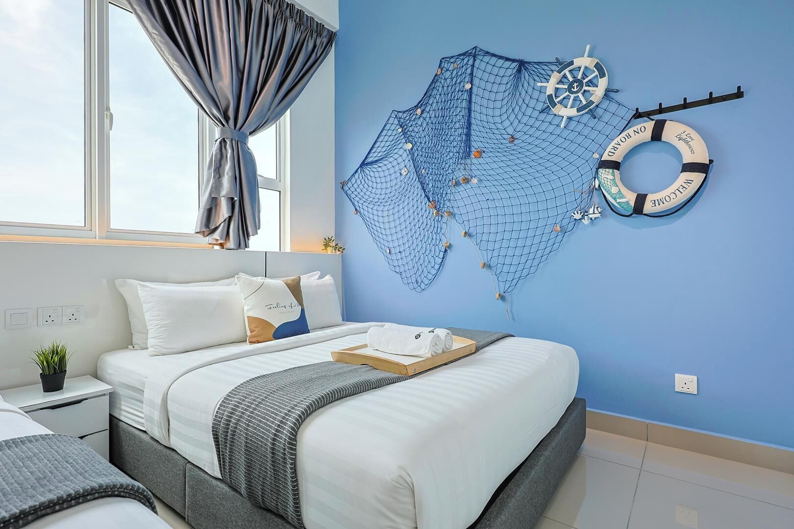 A bedroom with a bed, a nightstand, a potted plant, and a wall with a nautical-themed net and life ring.